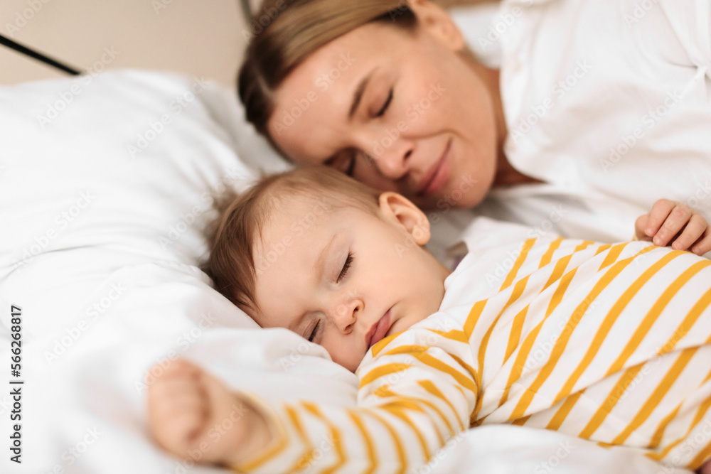 Bed-sharing with baby concept. Adorable infant child girl sleeping with her mother on bed in bedroom during daytime Bed-sharing with baby concept. Adorable infant child girl sleeping with her mother on bed in bedroom during daytime