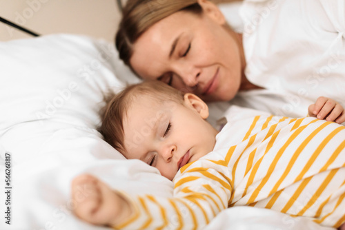 Bed-sharing with baby concept. Adorable infant child girl sleeping with her mother on bed in bedroom during daytime