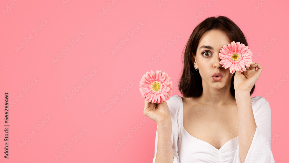Shocked young caucasian female puts flower to eye, enjoys free time, has fun