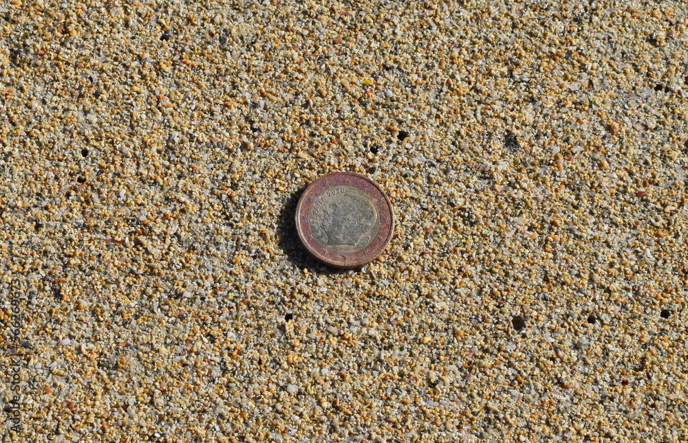 The lost coin lies on . One euro on sand background The lost coin lies on . One euro on sand background