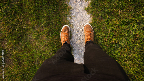 Top down to male feet on narrow path in grass, dressed in brown lace shows and black jeans | point of view | follow your path