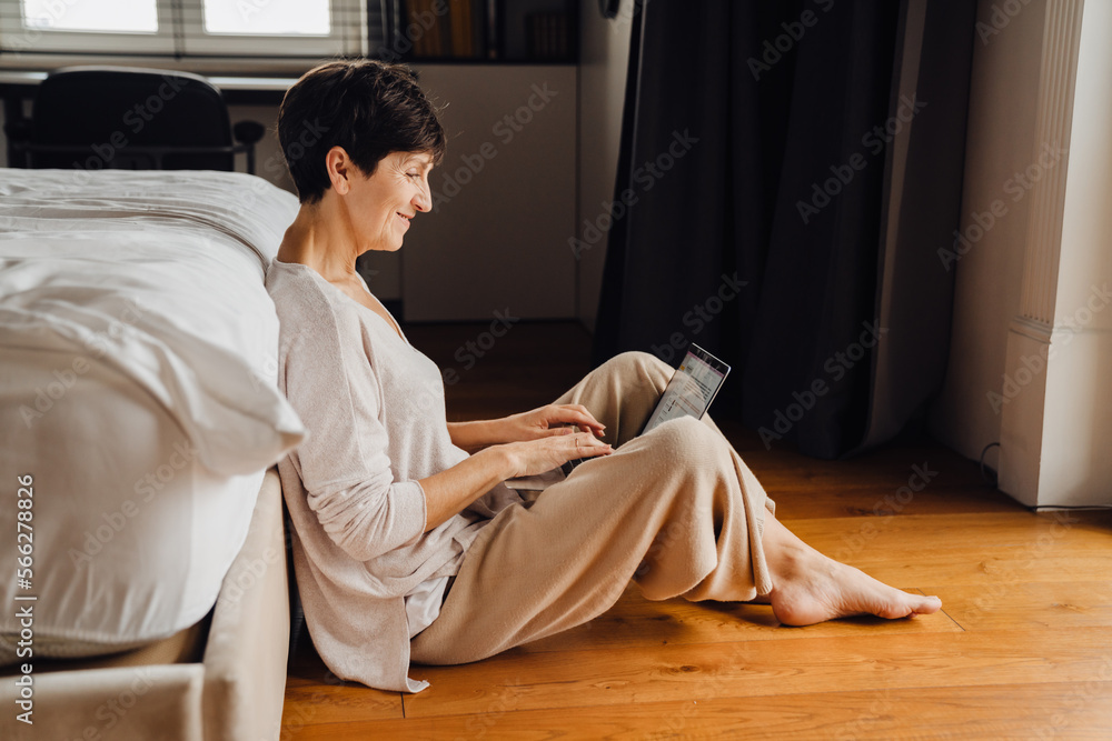 Smiling senior woman working on laptop while sitting in bedroom Smiling senior woman working on laptop while sitting in bedroom