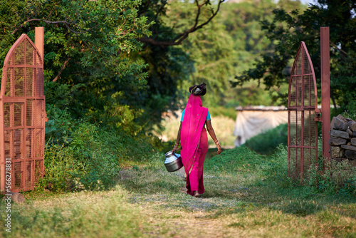 Obraz na płótnie A woman carries pots of food on her head through a green village w salonie