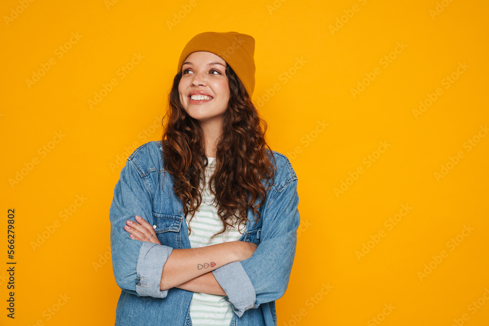 Cheerful young girl standing with arms folded isolated over yellow background