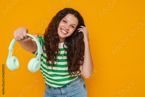 Young girl holding headphones isolated over yellow background
