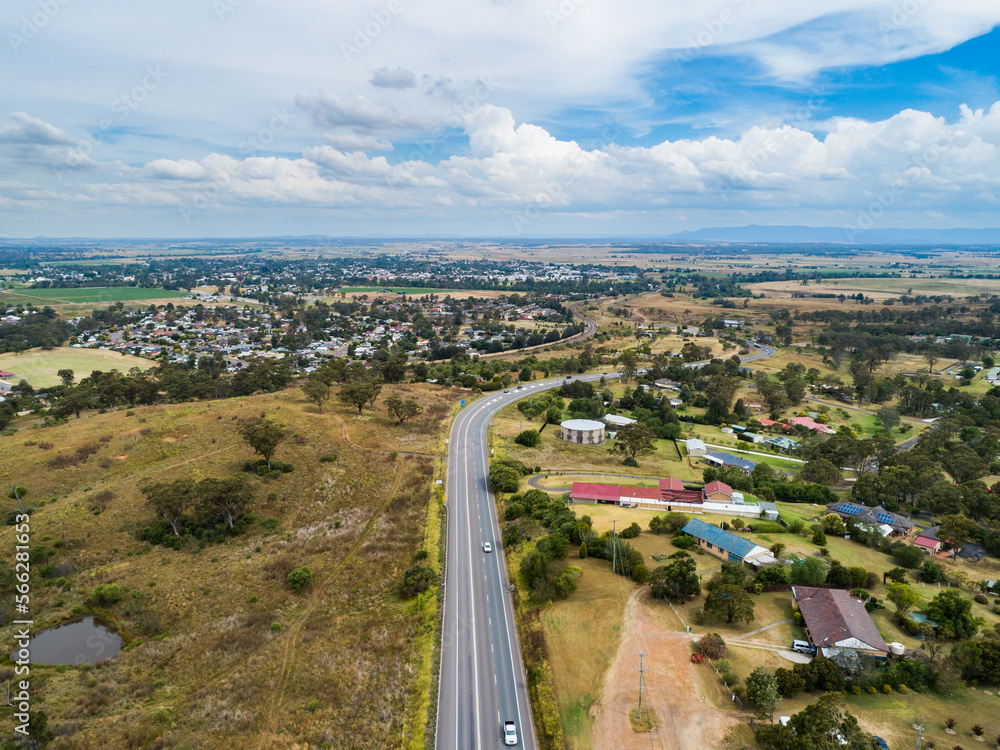 aerial view of road heading into town with properties and paddock beside aerial view of road heading into town with properties and paddock beside