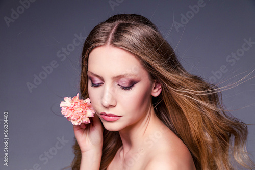 A beautiful young woman with shiny wavy brown hair. Model with healthy skin. Girl with a carnation flower.