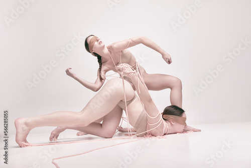 Inexplicit. Portrait of two young girls posing in underwear and ropes with eyes closed over light studio background. Concept of modern fashion, queer, art photography, weird people, creativity photo