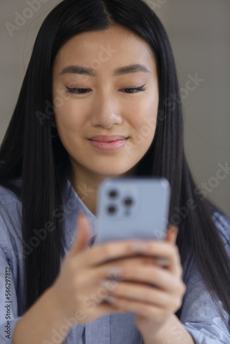 Portrait of beautiful Vietnamese BIPOC female typing sms message on smart phone. Cheerful Asian POC girl texting online with cellphone