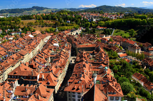 Panorama of the historic part of Bern with red-roofed houses, winding streets, arched bridge and church with mountains in the background 