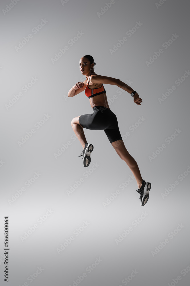 full length of brunette african american woman levitating during work out on grey.