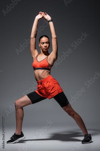 full length of young african american sportswoman in sneakers exercising with raised hands on grey.