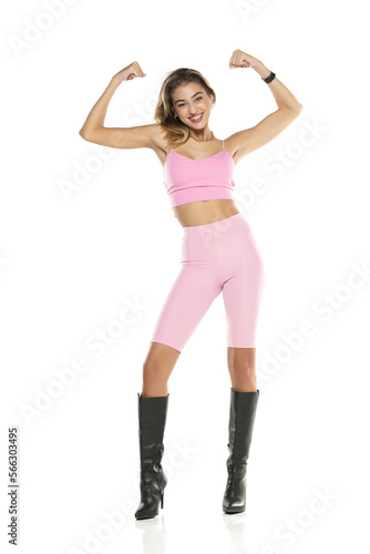 a young happy woman in pink short leggings and top, and black leather boots on a white background