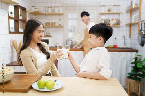 Asian cute little boy having a breakfast with his parent in a kitchen  boy holding a glass of milk and drink.
