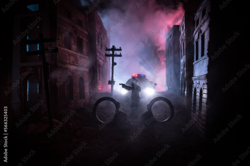 Police raid at night and you are under arrest concept. Silhouette of handcuffs with police car on backside. Image with the flashing red and blue police lights at foggy background. Slider shot