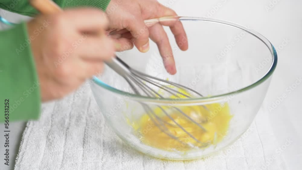 A man beats eggs with a hand whisk in a transparent bowl on the kitchen table. High quality 4k footage A man beats eggs with a hand whisk in a transparent bowl on the kitchen table. High quality 4k footage