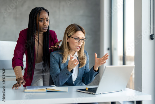 Wall Mural Two multiethnic business women in suit having problems with laptop, system being hacked stopped working lost internet connection in middle of important work, feeling frustrated over deleted lost data