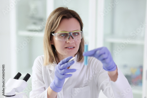 Gloved female scientist in glasses looking at sample while doing research in laboratory.