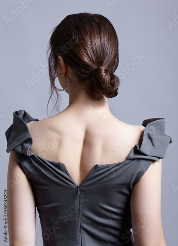 Young woman with unzipped zipper on the dress. Bunette female rear view with hair knot and earrings in the ears.