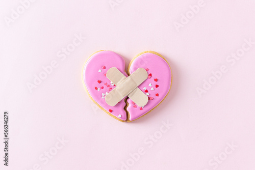 Broken heart with plaster concept. Divorse, quarrel, break. reunion. Broken cookie in heart shape on pink background. Family psychotherapist, heal menthal problems. heartbreak, loss concept. photo