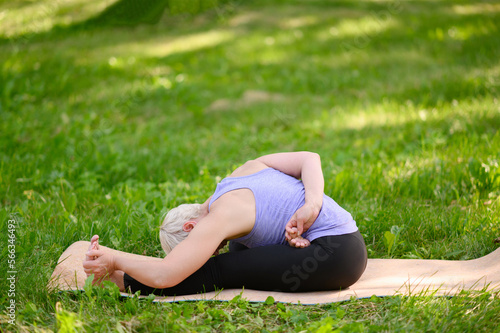 Middle-aged woman doing yoga in the park, sitting in the Janu Sirshasana exercise, Head to Knee Pose