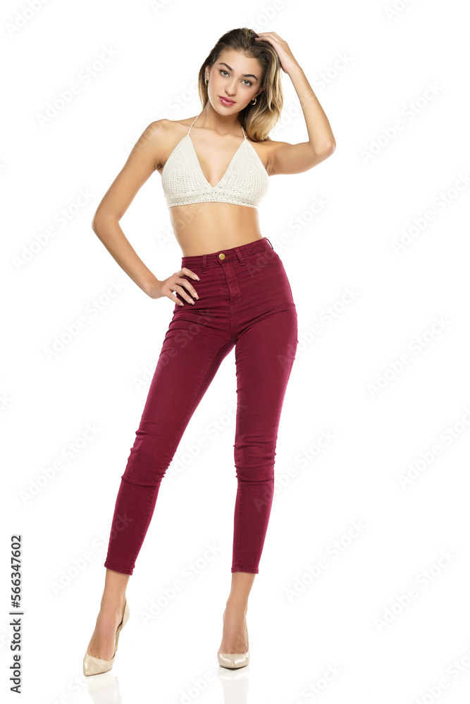 a young woman in burgundy jeans and top, and high heels shoes posing on a white background a young woman in burgundy jeans and top, and high heels shoes posing on a white background