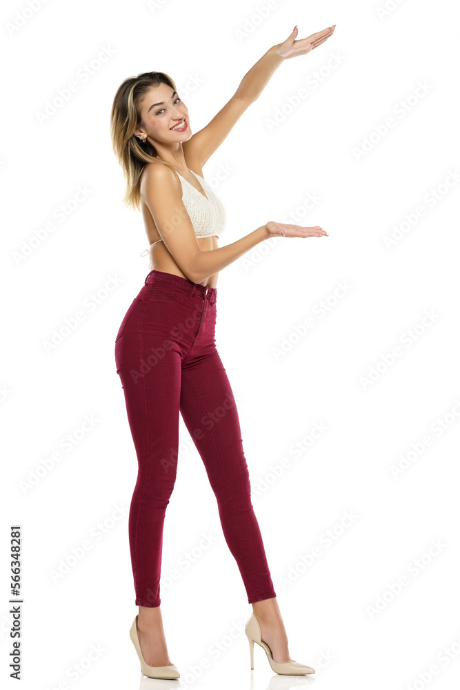 Smiling Woman In Burgundy Jeans And Top Presenting Something On her Empty Palm On A White Background Smiling Woman In Burgundy Jeans And Top Presenting Something On her Empty Palm On A White Background