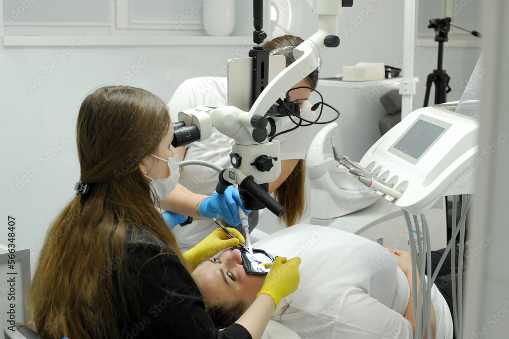 process of dental treatment prosthetics filling canals using a microscope female doctor in yellow gloves patient assistants nurse latest technologies in dentistry Dentist office with modern equipment process of dental treatment prosthetics filling canals using a microscope female doctor in yellow gloves patient assistants nurse latest technologies in dentistry Dentist office with modern equipment
