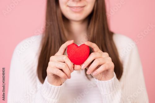 girl holding a heart in her hands close-up on a pink background, the concept of valentine's day