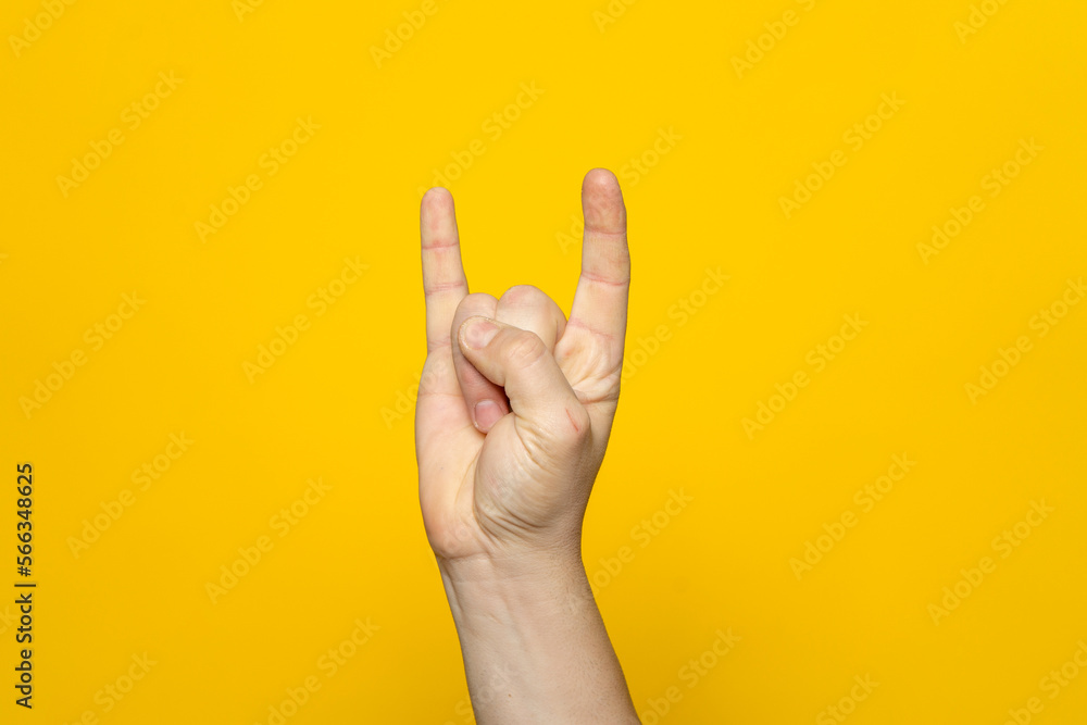 Naklejka premium Strong hand of man making the rock gesture on a yellow studio background.