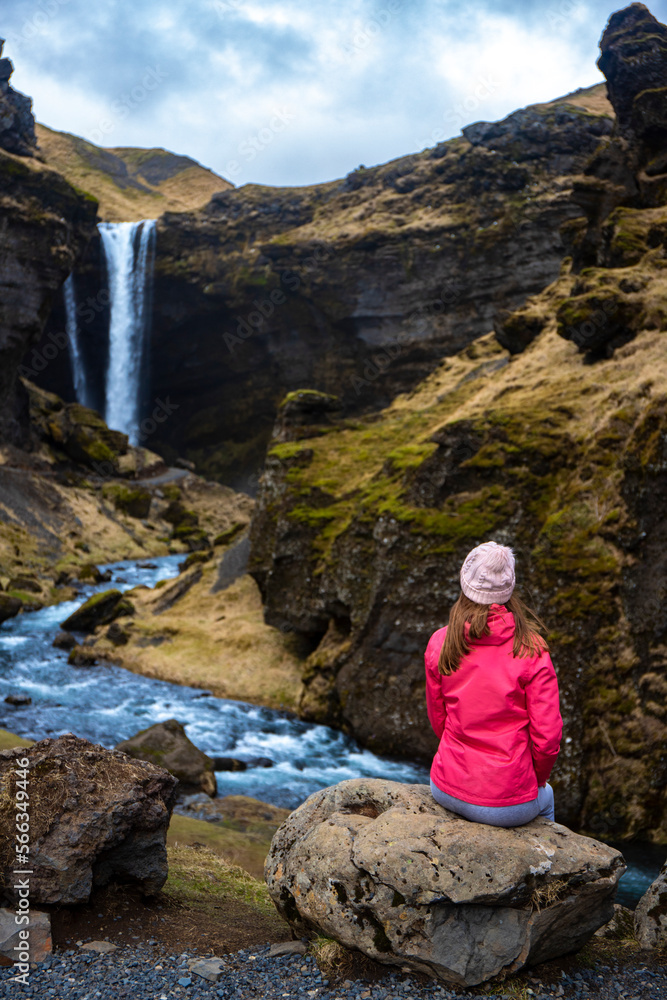 Girl in pink jacket admires stunning famous Kvernufoss waterfall and river hidden in canyon in picturesque setting, Iceland