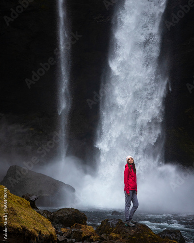 beautiful young brave girl in pink jacket stand close to famous powerful Kvernufoss waterfall in southern Iceland, Europe, spring. 