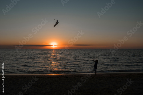 happy girl running with a kite at sunset outdoors. A child runs with a kite at sunset against the backdrop of the sea. Family vacation. High quality photo.
