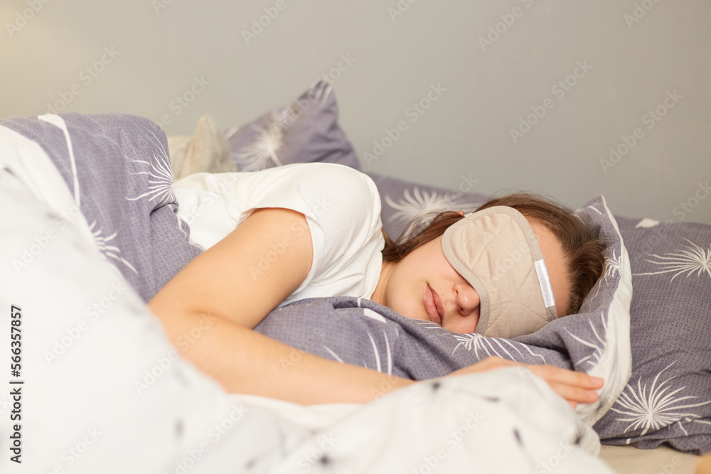 Side view portrait of cute dark haired woman in her bed in white pajama and sleep mask, sleeping on weekend, resting on her day off, laying under blanket. Side view portrait of cute dark haired woman in her bed in white pajama and sleep mask, sleeping on weekend, resting on her day off, laying under blanket.