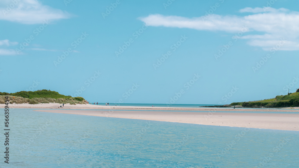 Clear cloudless sky over a beautiful sandy beach. A few people on a sandy beach. Picturesque seascape of Ireland on a summer day. A copy space. People walking on beach