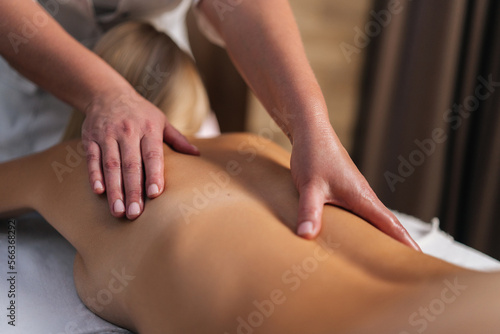Cropped shot of unrecognizable male masseur doing back and shoulder massage to female client with beautiful skin lying in spa salon. Male masseur professionally massaging young woman client.