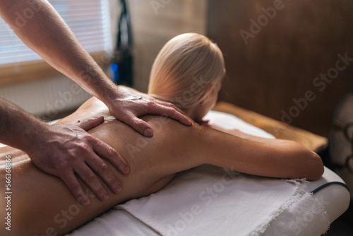 Cropped shot of unrecognizable male masseur doing back massage to naked female client in spa salon lying on massage table. Concept of body care and rehabilitation of spiritual peace.