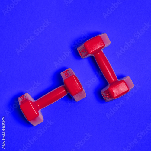 Two bright red dumbbells are isolated on blue background. Sport and health concept. photo