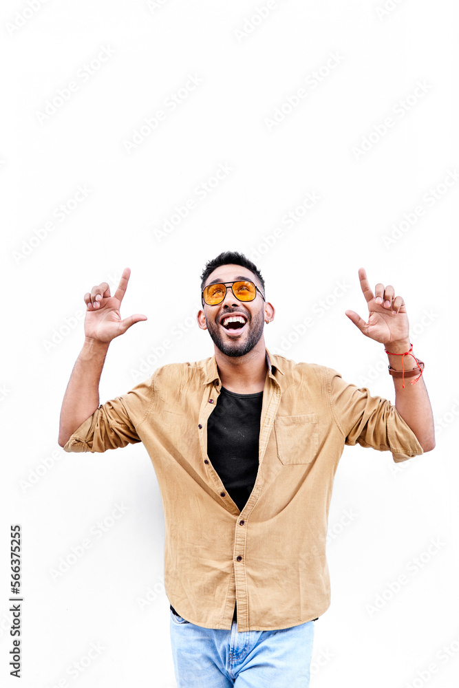Naklejka premium smiling happy young Hispanic-Latino ethnic pointing with both hands upwards on white isolated background. copy space for text. vertical photograph.