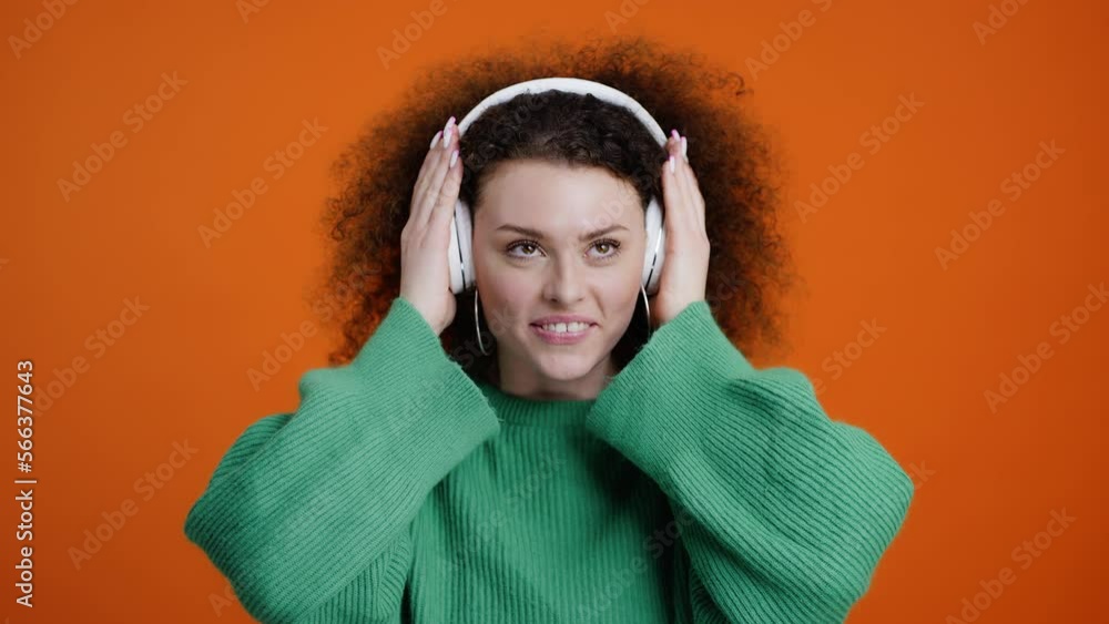 Charming young woman putting on headphones and enjoying listening to the music on orange background Charming young woman putting on headphones and enjoying listening to the music on orange background