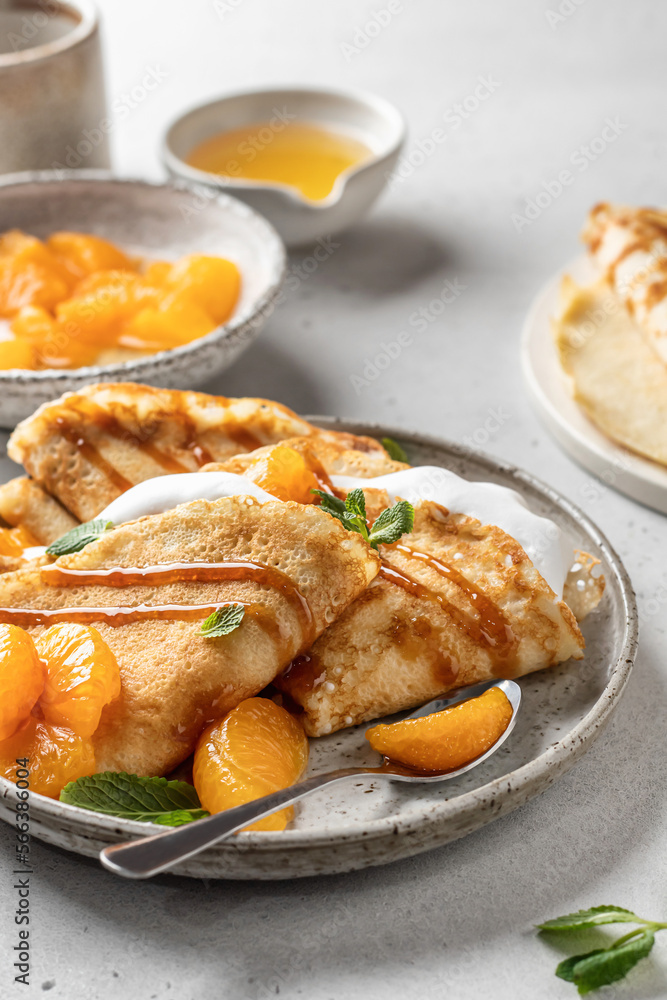 Crepes with fresh mandarin, caramel, cream in the filling and mint leaves on white textured background. Maslenitsa or Pancake week traditional concept