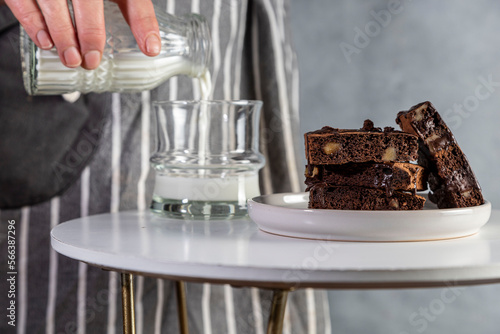 Healthy gluten free chocolate brownie in a plate with nuts and cocoa powder. Homemade, freshly baked delicious brownies in the background and woman's hand takng one. Nutrition concept photo