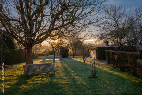 Alencon, France - 01 27 2023: sunset in a garden by the river with trees, lampposts and wooden bench © Franck Legros