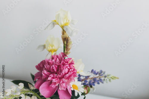 Modern summer flowers still life arrangement on white wall background with space for text. Creative floral greeting card. Stylish peony  lupin  iris and daisy composition