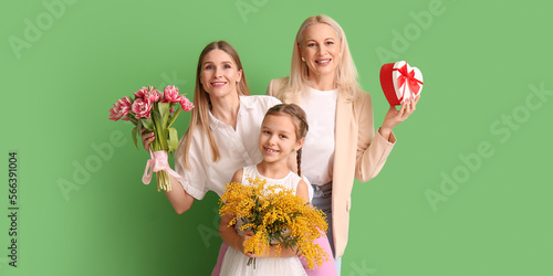 Young woman, her little daughter and mother with gifts on green background. International Women's Day