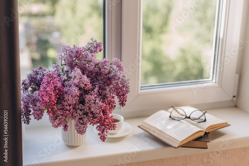 Bouquet of lilacs in a vase,cup of coffee and books on the windowsill.