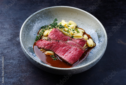 Traditional Italian chianina sliced roast beef with gnocchetti sardi pasta in spicy red wine sauce served as close-up in a Nordic design bowl with copy space