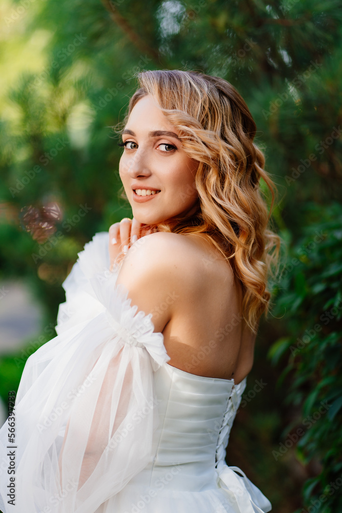 a bride in an open-shouldered dress poses against the backdrop of greenery a bride in an open-shouldered dress poses against the backdrop of greenery