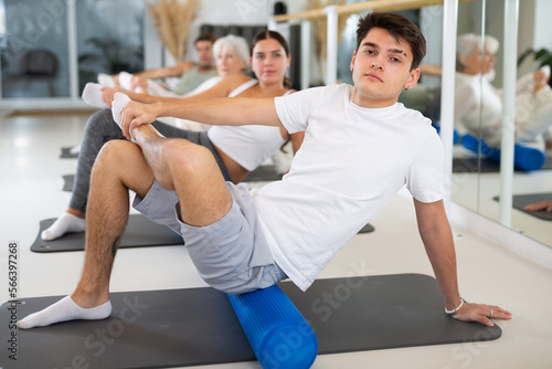 Sporty slender males and females doing exercises with pilates roller during group training at gym. Healthy lifestyle concept.