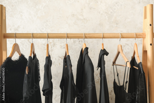 Rack with black female clothes near light wall